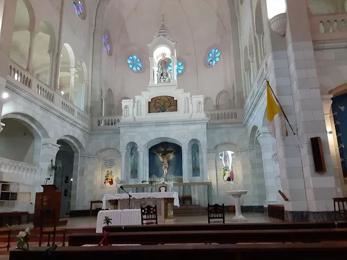 Interior del templo: altar mayor con el crucifijo al centro y el retablo blanco detrás, visto desde los bancos