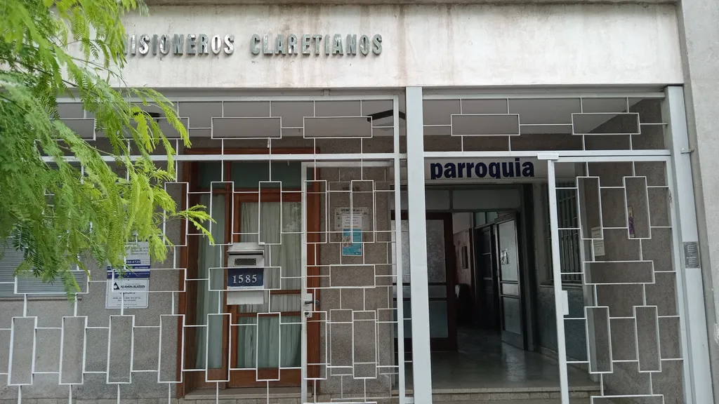 Entrada a la secretaría: puerta con reja blanca bajo el cartel «Misioneros Claretianos», con el número 1585 y el letrero «parroquia» sobre el pasillo